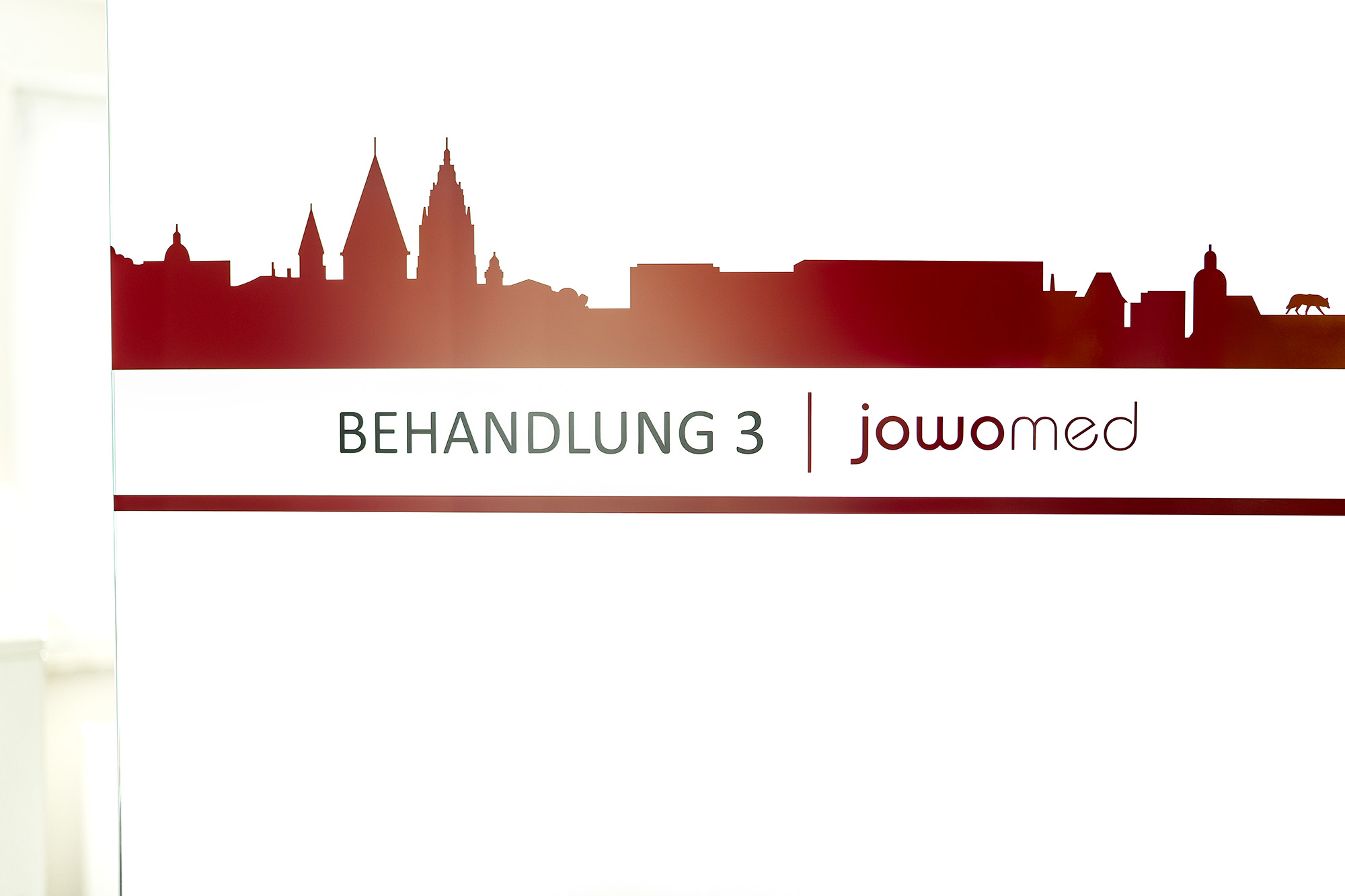 Praxisschild „Behandlung" mit Blick auf die Mainzer Skyline in der Praxis Jochen Wolf & Kollegen