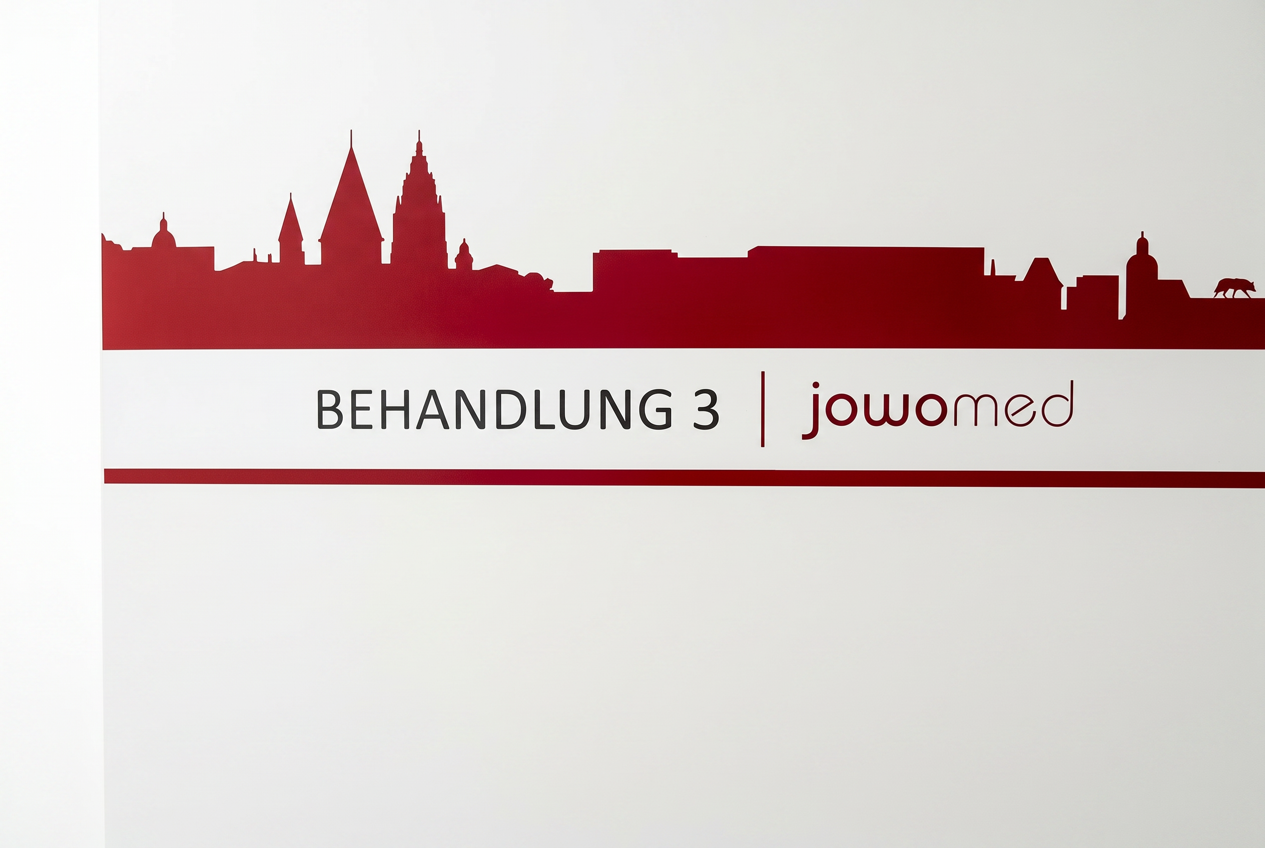 Praxisschild „Behandlung" mit Blick auf die Mainzer Skyline in der Praxis Jochen Wolf & Kollegen